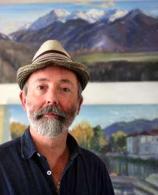 Portrait de Robin Spencer, chapeau de paille, devant ses toiles.